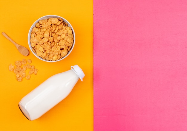 Top view of cornflakes and milk with copy space on pink and yellow background horizontal