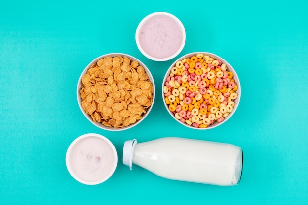 Top view of cornflakes and milk with yogurt on blue surface horizontal