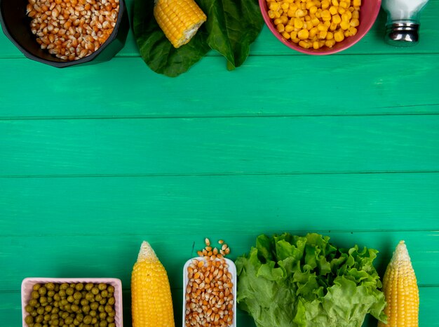 Top view of corns and corn seeds with green peas salt lettuce spinach on green with copy space