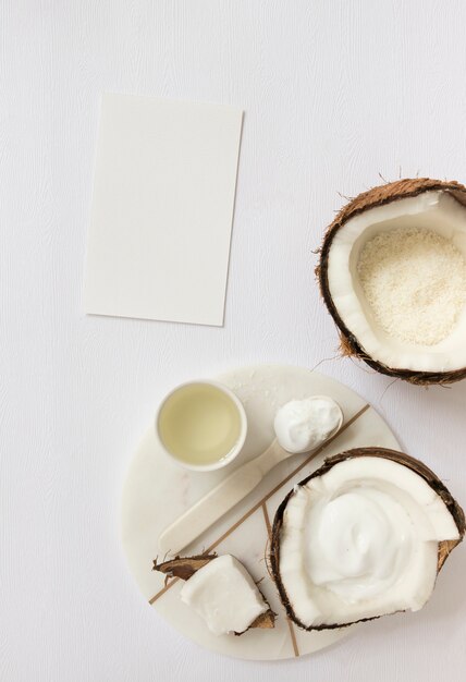 Top view of cosmetic with coconut and blank card on white surface