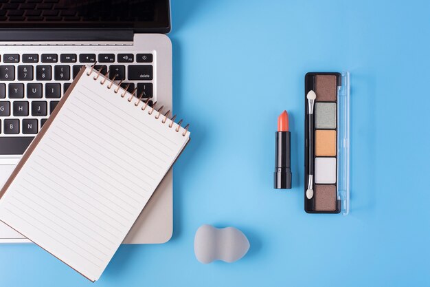 Top view of cosmetics and laptop on blue background