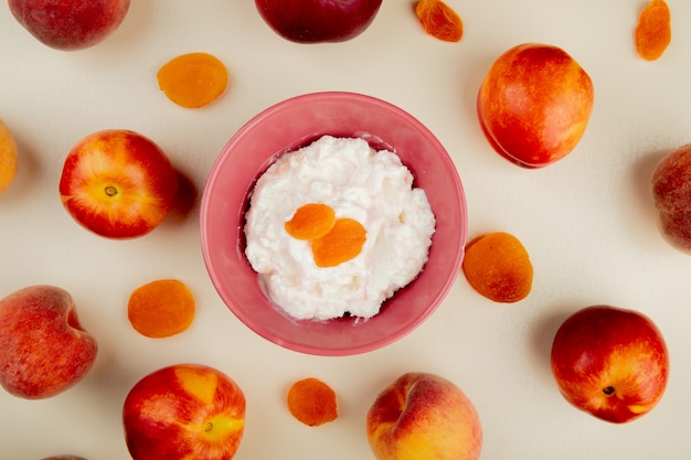 Top view of cottage cheese in a bowl and fresh sweet nectarines and peaches with dried apricots on white