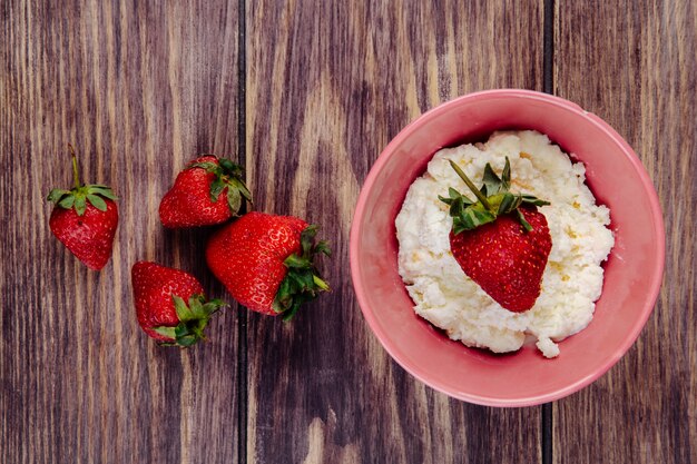 top view of cottage cheese in a pink bowl and fresh ripe strawberries on rustic wooden surface