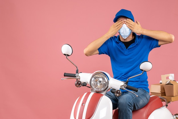 Top view of courier guy in medical mask wearing hat sitting on scooter delivering orders closing his eyes on pastel peach background