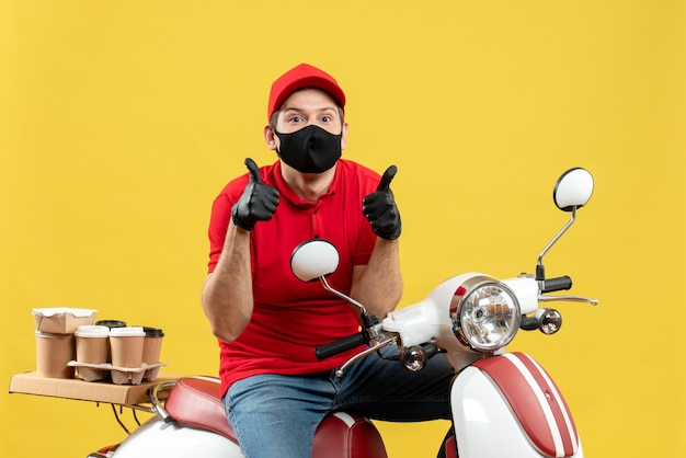 医療用マスクで赤いブラウスと帽子の手袋を着用している宅配便の男の上面図は、スクーターに座って注文を配信します。