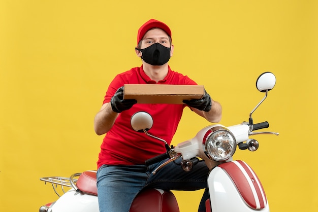 Vista dall'alto del corriere uomo che indossa camicia rossa e guanti cappello in mascherina medica che si siede sul motorino che dà ordine