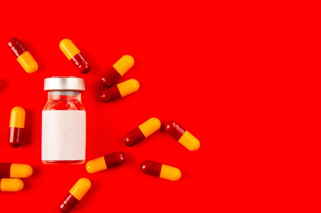 top view covid vaccine inside little flask with pills on red background