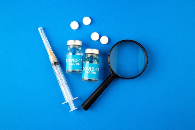 вид сверху вакцина против covid с инъекцией лупы и таблетками на синем фоне больница здоровье covid- lab наука лекарство от пандемического вируса