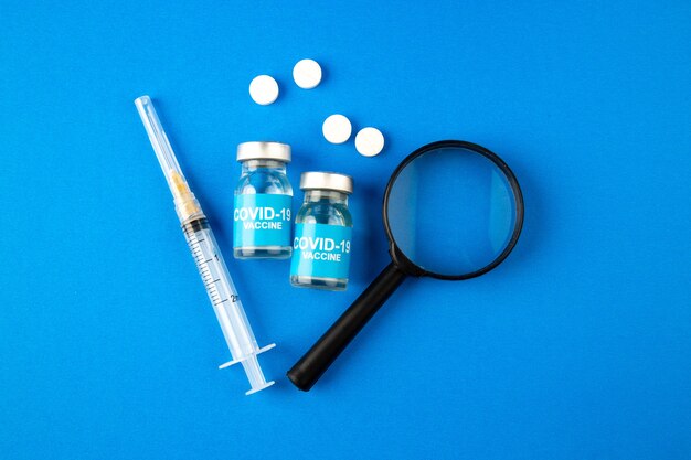 top view covid vaccine with magnifier injection and pills on blue background hospital health covid- lab science pandemic virus drug