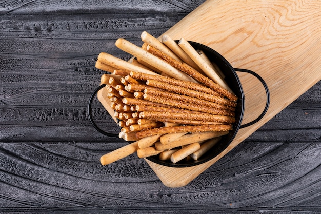 Top view of crackers in black pan and wooden cutting board on dark  horizontal