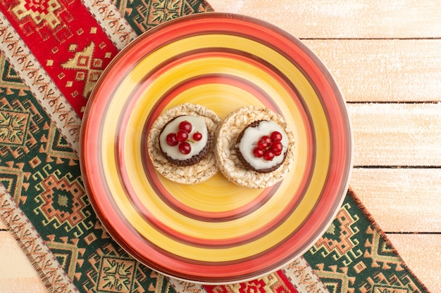 Top view of crackers and cakes with cranberries on top inside colored plate
