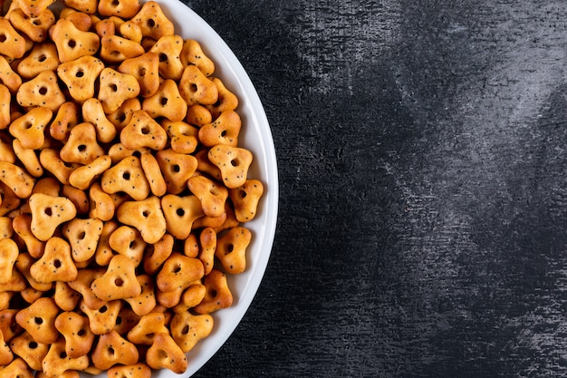 Top view crackers in white bowl with copy space on right on black stone  horizontal