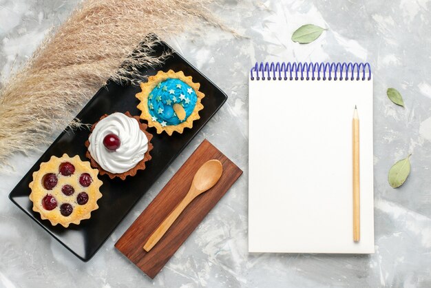 Top view of cream cakes with frutis along with notepad on grey-light desk, cake biscuit sweet sugar