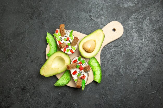 Top view of creamy avocados with bread and pepper and fresh avocados on a grey surface