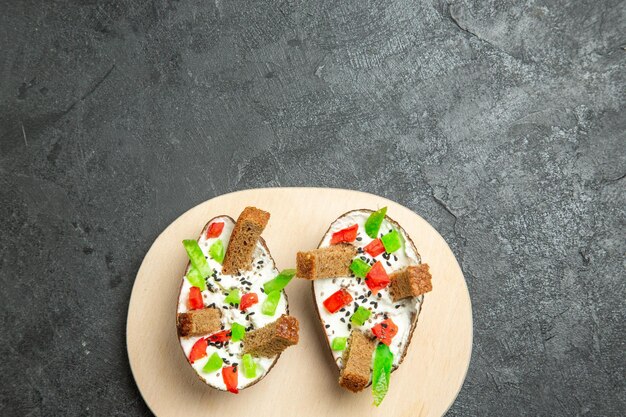 Top view of creamy avocados with sliced peppers and bread pieces on a grey surface