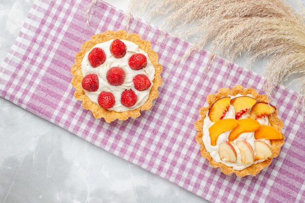Вид сверху на кремовые пирожные с белым вкусным кремом и нарезанной клубникой, персиками, абрикосами на свете, выпечка с фруктовым кремом