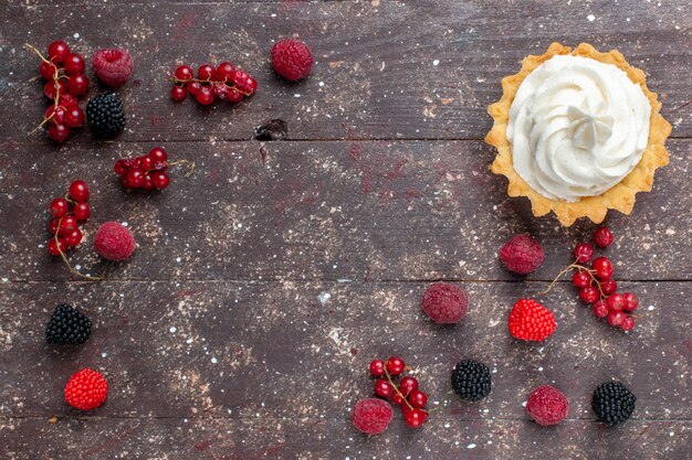 Free photo top view of creamy delicious cake along with differented berries spread all over the brown, fruit cream bake biscuit