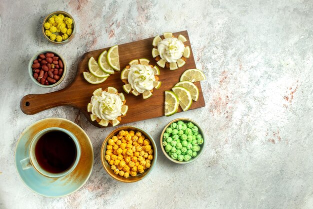 Top view creamy delicious cakes with lemon slices candies and tea on white surface cake biscuit cookie sweet cream tea