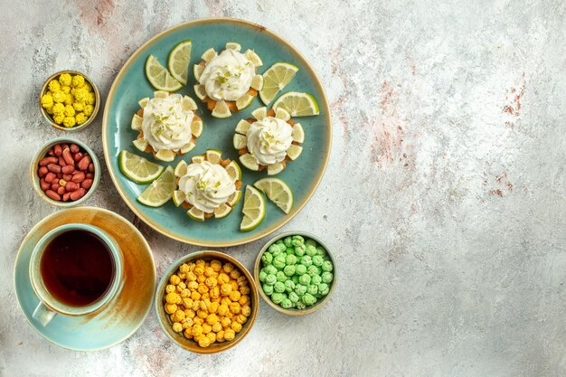 Вид сверху кремовые вкусные пирожные с дольками лимона и чашкой чая на белой поверхности торт бисквитное печенье крем чай сладкий