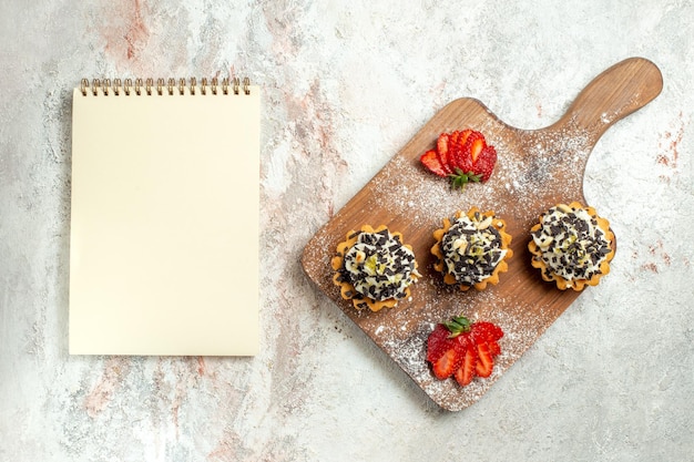 Free photo top view creamy delicious cakes with sliced strawberries on a white surface cream tea cake biscuit birthday sweet