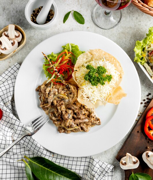 Top view of creamy meat slices with mushroom served with rice and salad