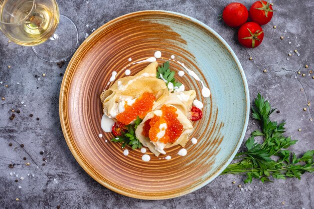 Top view of crepes with red caviar and cream garnished with parsley