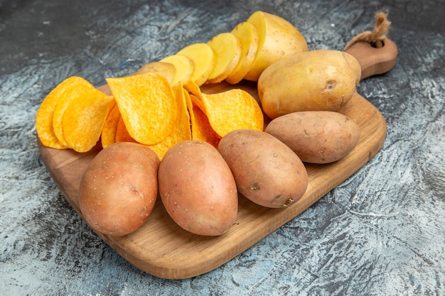 Free photo top view of crispy chips and uncooked potatoes on wooden cutting board on gray background