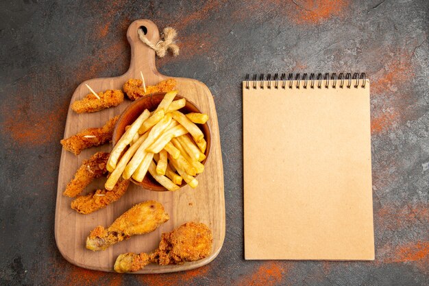 Вид сверху хрустящего жареного картофеля и курицы на деревянной разделочной доске