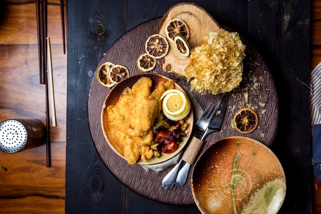 Top view of crispy fried fish served with lemon, fries and vegetable salad