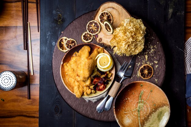 Top view of crispy fried fish served with lemon, fries and vegetable salad