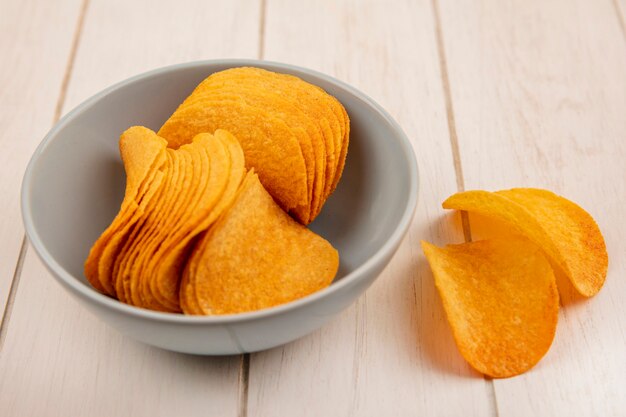 Top view of crispy potato chips on a bowl on a beige wooden table