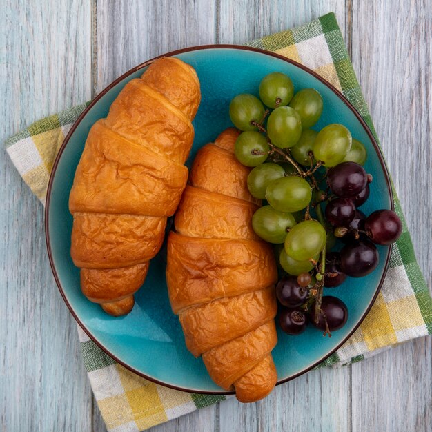 Top view of croissants with grapes in plate on plaid cloth on wooden background