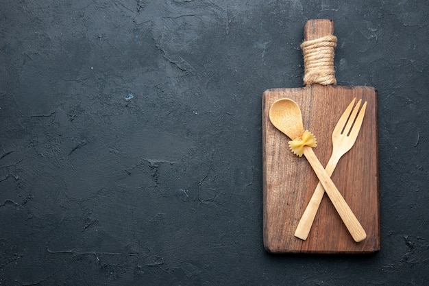 Top view crossed wooden spoon and fork on wooden serving board on black table copy place