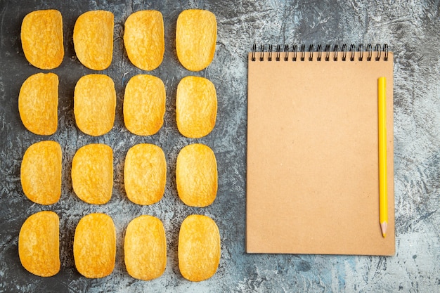 Top view of crunchy baked five chips lined up in rows and notebook with pen on gray background