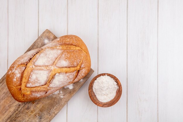 Top view of crusty bread on cutting board and bowl of flour on wooden background with copy space