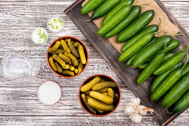 Top view cucumber pickled in bowls on beige linen bag on wooden tray on white wooden