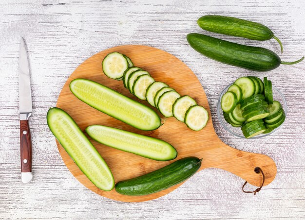 Top view cucumber sliced in glass bowl on beige cutting board on white wooden  horizontal