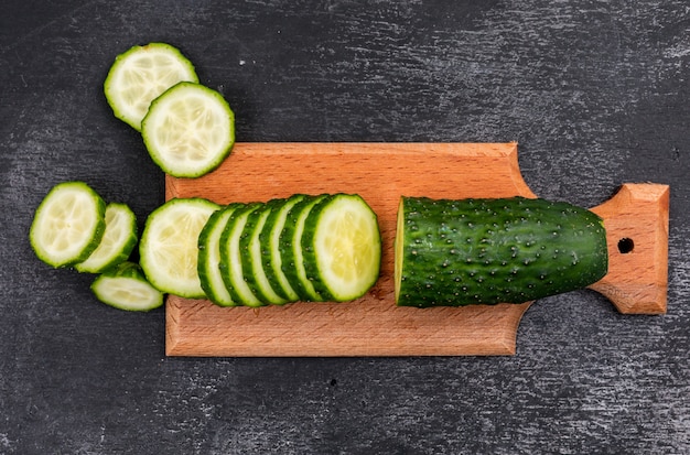 Top view cucumber sliced on wooden cutting board on black stone  horizontal
