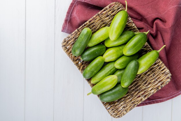 Top view of cucumbers in basket plate on bordo cloth on right side and wooden surface with copy space