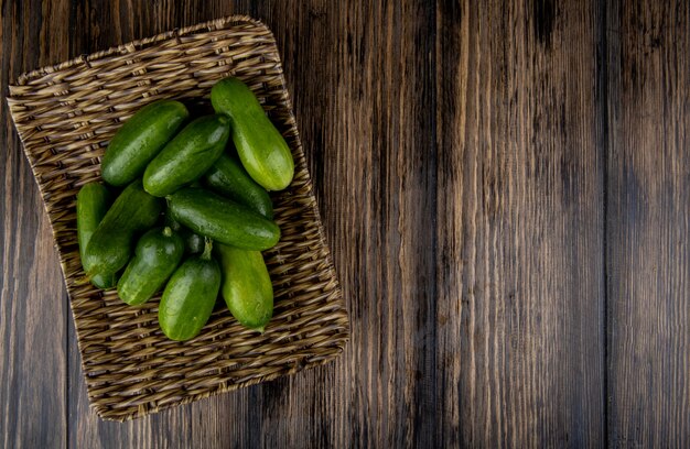 Top view of cucumbers in basket plate on wooden surface with copy space