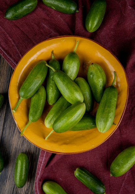 Top view of cucumbers in plate with other ones on bordo cloth and wood