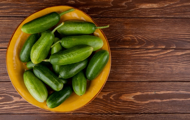 Top view of cucumbers in plate on wooden surface with copy space