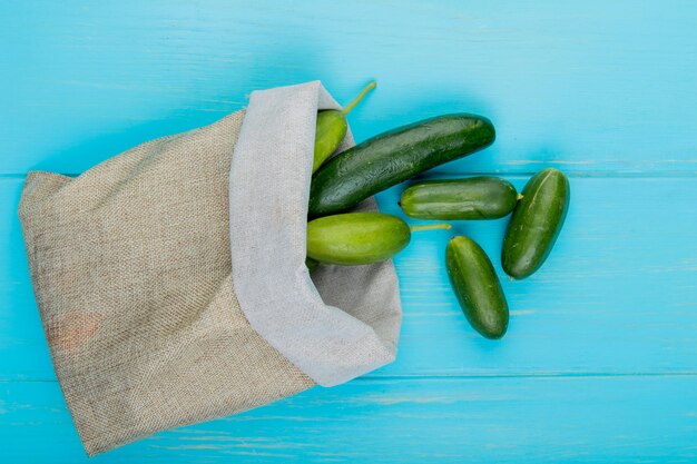 Top view of cucumbers spilling out of sack on blue surface