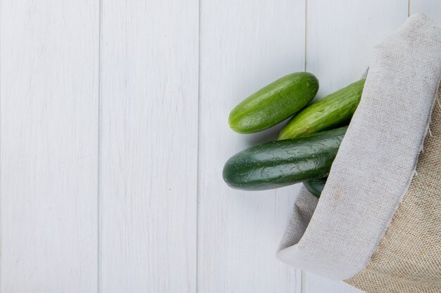 Top view of cucumbers spilling out of sack on right side and wooden surface with copy space