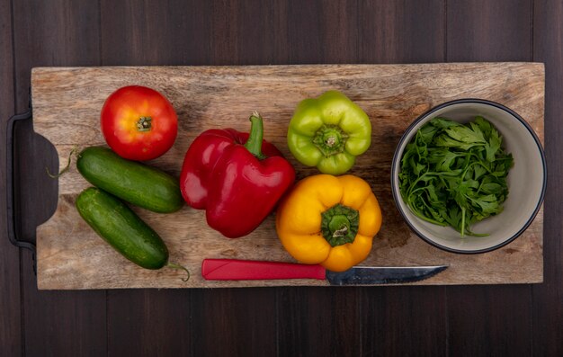 Top view cucumbers with bell peppers on a cutting board with parsley in a bowl on a wooden background