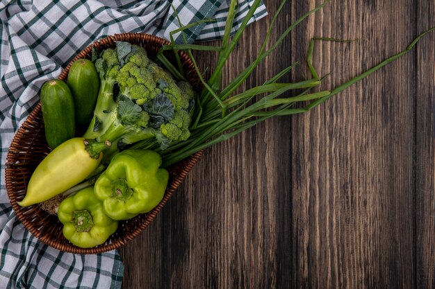 Top view cucumbers with green peppers  broccoli and green onions in basket on wooden background