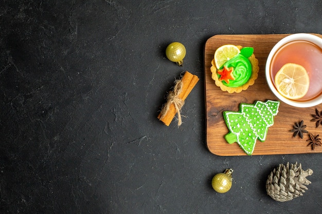 Top view of a cup of black tea wit lemon new year accessories conifer cone and cinnamon limes on black background