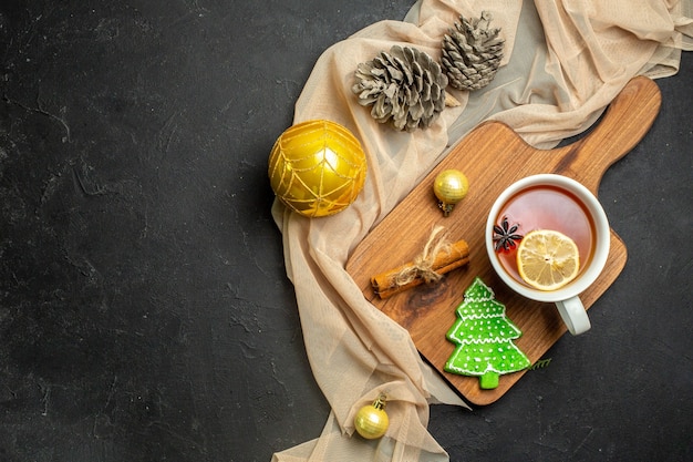 Top view of a cup of black tea with lemon and cinnamon limes new year decoration accessories on wooden cutting board on nude color towel