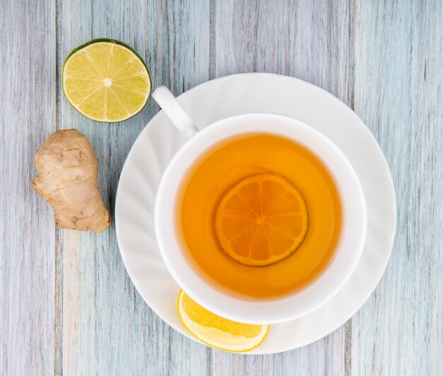 Top view of a cup of black tea with lemon slices with ginger on grey wood