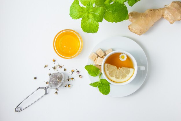 Вид сверху чашку ромашкового чая с травами, мед, листья мяты, сахар на белой поверхности. горизонтальный